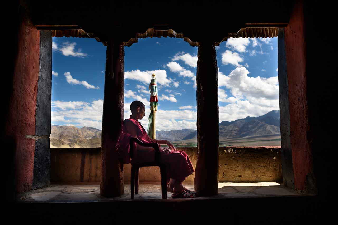 Monk sitting and looking at the landscape outside, Ladakh