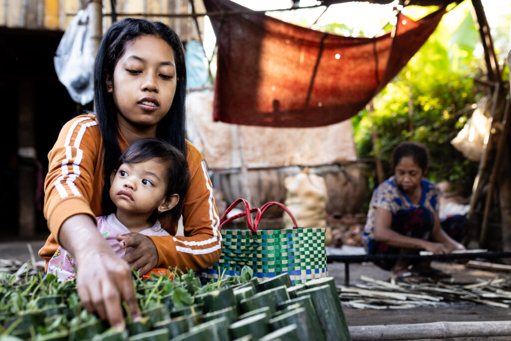 From close proximity, a woman making bamboo sticky rice in Cambodia, captured with 35mm to show context and layers.